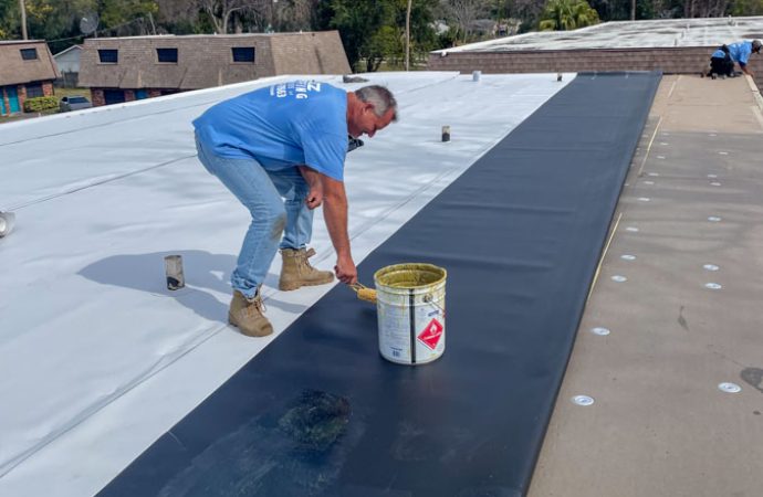Roofer applying sealant on a commercial flat roof to ensure waterproofing, demonstrating attention to detail and expertise in roofing maintenance.