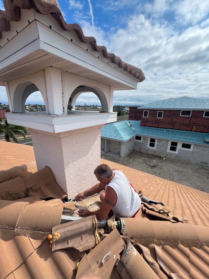 Roofer repairing tiles near chimney on residential roof