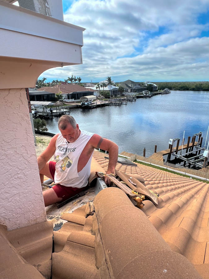 A roofer inspects and repairs clay tiles on a steep roof, emphasizing safety and skill in roof maintenance tasks.